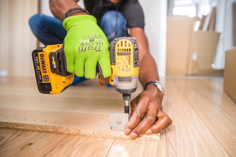 Hand in a work glove driving a screw with a power drill into wood