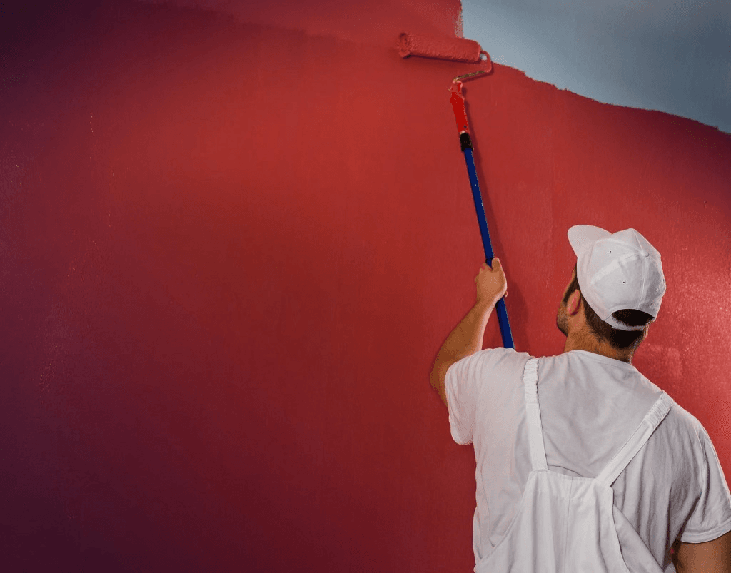 Painter in overalls using a roller to paint an interior wall